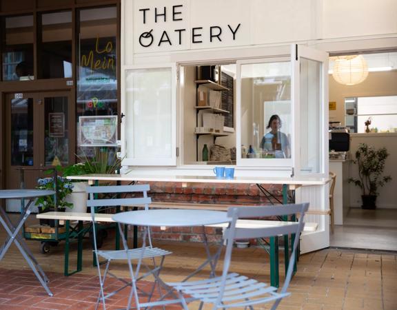 The white exterior of The Oatery, with light blue tables and chairs outside.