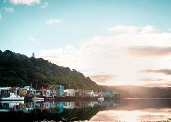 A scenic shot of Tītahi Bay in Porirua, with the sun rising over the hills in the background and boatsheds on the water.