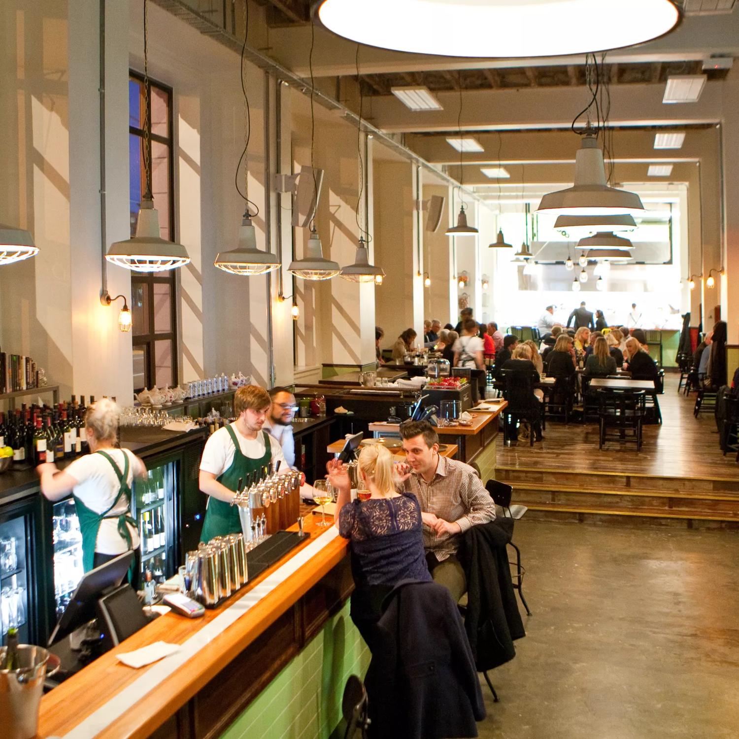 Inside Charley Noble during a busy dinner service. The restaurant has high ceilings, lanterns, and large windows along the left wall.