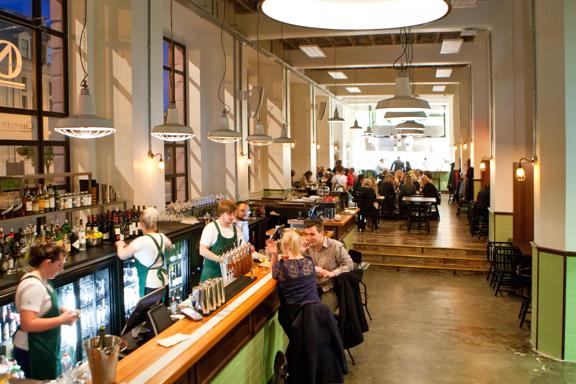 Inside Charley Noble during a busy dinner service. The restaurant has high ceilings, lanterns, and large windows along the left wall.