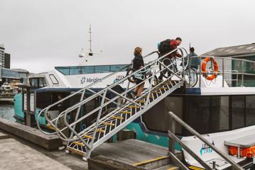 Two people carrying their bicycles as the aboard The Ika Rere electric ferry at the Wellington waterfront.