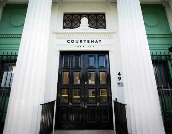 The front facade of the Courtenay Creative building in Te Aro, Wellington. Located at 49 Courtenay Place and its' walls are white and green with a large black door.  