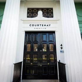 The front facade of the Courtenay Creative building in Te Aro, Wellington. Located at 49 Courtenay Place and its' walls are white and green with a large black door.  