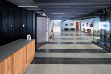 The Tiakiwai Foyer has grey titles, a low ceiling and glass walls.