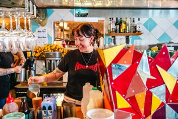 A waiter inside Seashore Cabaret is pictured smiling while pouring a coffee. Vibrant colours decorate the room.