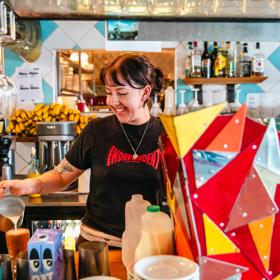 A waiter inside Seashore Cabaret is pictured smiling while pouring a coffee. Vibrant colours decorate the room.