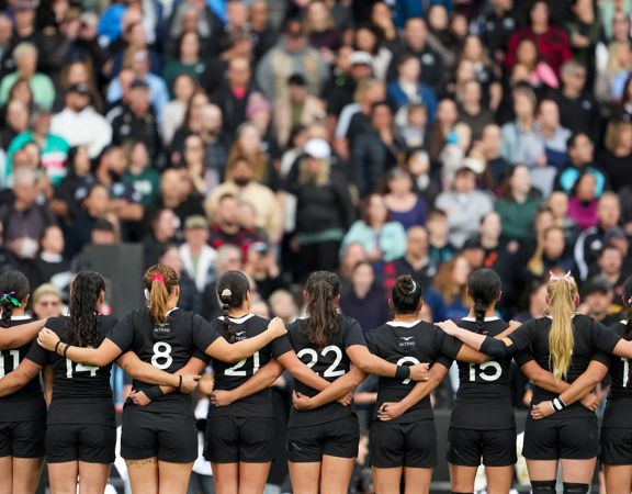 Black Ferns rugby players standing in a line with their hands crossing over each other.