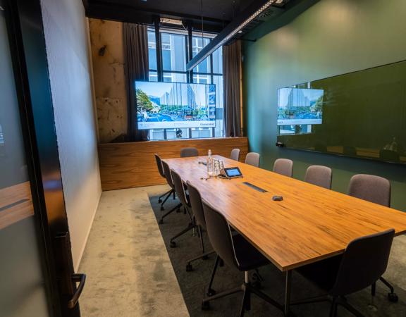 A meeting room at Generator on Waring Taylor Street has green walls, a wooden table surrounded by 12 chairs.