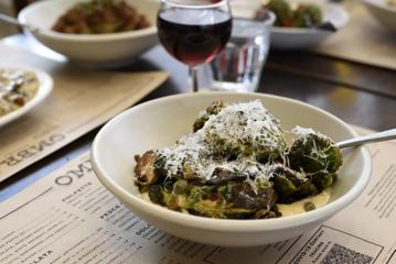 A dish with Brussels sprouts topped with parmesan cheese and a glass of red wine on a table.