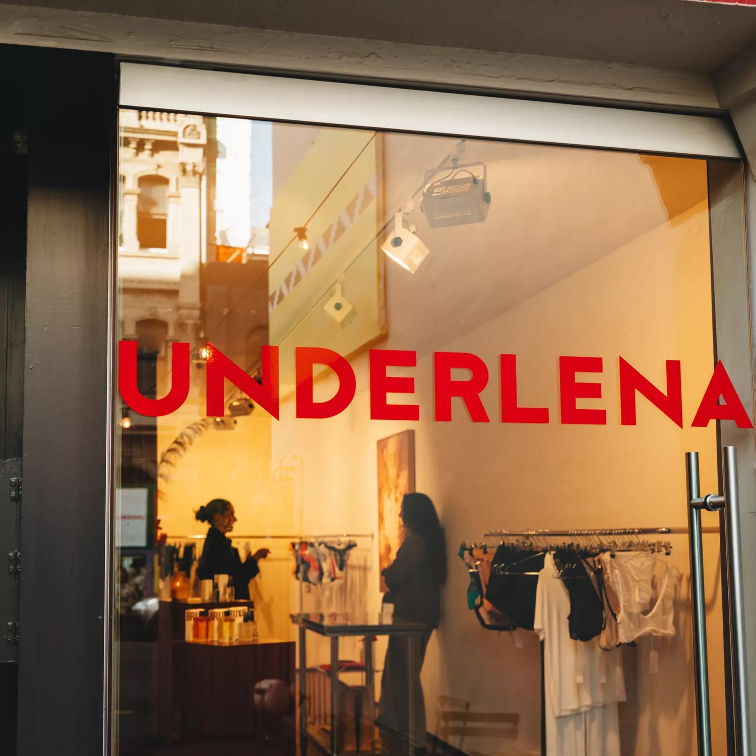 Looking into the glass front doors at Underlena, a lingerie store in Te Aro Wellington, two people are shopping inside.