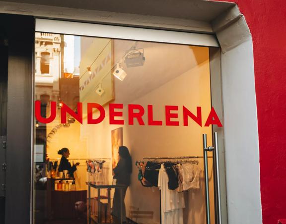 Looking into the glass front doors at Underlena, a lingerie store in Te Aro Wellington, two people are shopping inside.