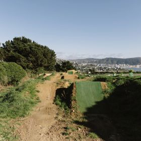 Dirt mountain bike jump tracks lined with synthetic grass, and Wellington city in the background.