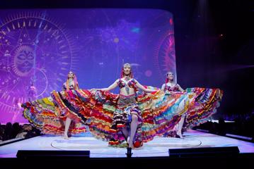 Three models wearing colourful flowing dresses on stage at the World of WearableArt show in Wellington, New Zealand.