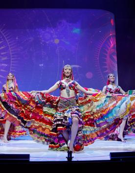 Three models wearing colourful flowing dresses on stage at the World of WearableArt show in Wellington, New Zealand. 