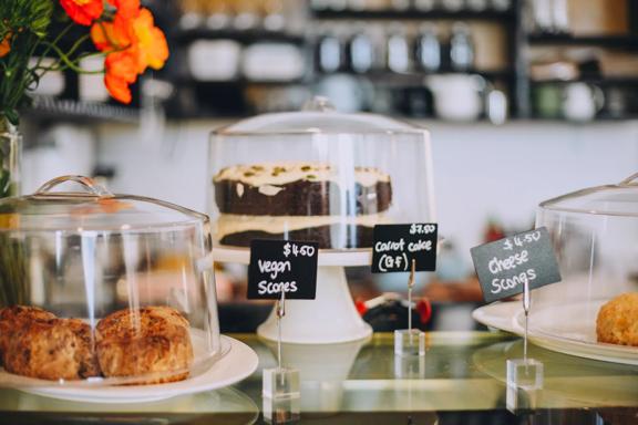 Cheese scones, carrot cake, and vegan scones underneath glass covers in t bay cafe Porirua.