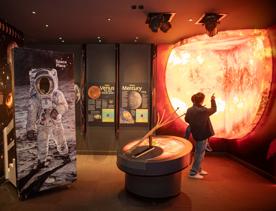 A parent and child pointing at the glowing sun exhibition inside Space Place.