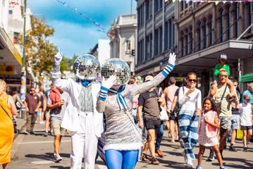 Two street performers dresses in silver and blue with disco balls on their heads are dancing and waving as a part of the CubaDupa street festival in Wellington.