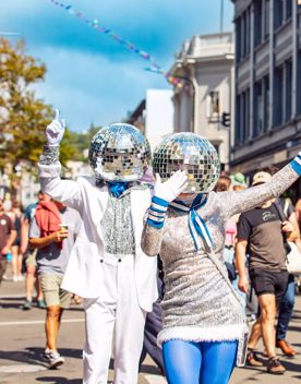 Two street performers dresses in silver and blue with disco balls on their heads are dancing and waving as a part of the CubaDupa street festival in Wellington.