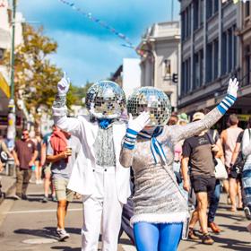 Two street performers dresses in silver and blue with disco balls on their heads are dancing and waving as a part of the CubaDupa street festival in Wellington.