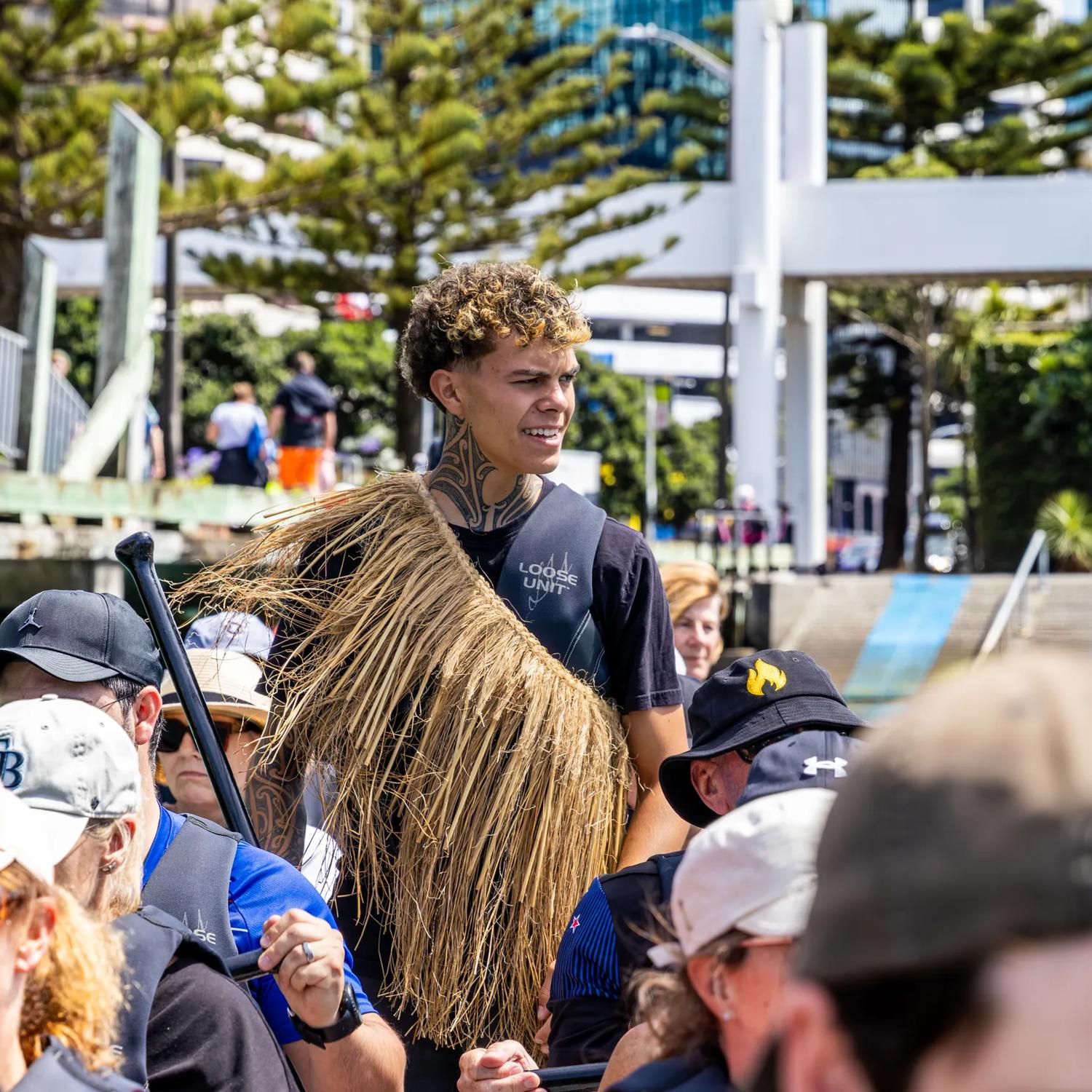 A waka experience guide stands in the middle of people rowing at Whairepo Lagoon on Wellington's waterfront.