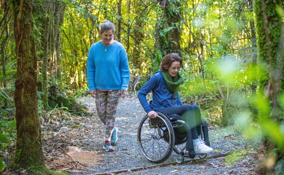 Two people are on a nature trail, one is a wheelchair user. 