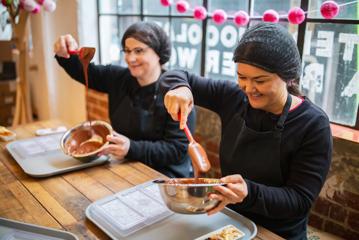 Two people are mixing melted chocolate in silver bowls at Wellington Chocolate Factory located in Te Aro, Wellington.