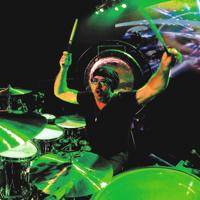 Jason Bonham plays the drums under neon green stagelights.