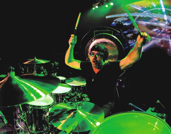 Jason Bonham plays the drums under neon green stagelights.