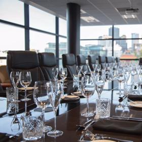 A conference room with a huge table, set with dinner-wear and big leather office chairs.