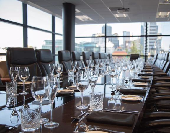 A conference room with a huge table, set with dinner-wear and big leather office chairs.