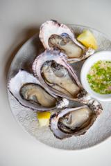 A plate with four oysters two lemon wedges and a small bowl of mignonette at Ortega Fish Shack, a seafood restaurant in Wellington, New Zealand.