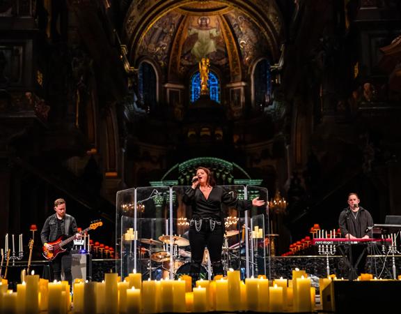 Three musicians wearing all-black perform by candlelight at a church.