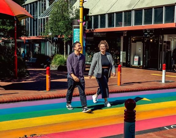 Two people cross the street at the Rainbow Crossing on Cuba Street in Te Aro, Wellington.