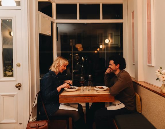 A couple on a dinner date enjoy food and wine at a small table by the front window at Rita, a small restaurant in Aro Valley, Wellington.