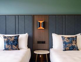 2 single beds sit either side, with a bedside table and lamp in the middle, inside The Sebel, Lower Hutt.