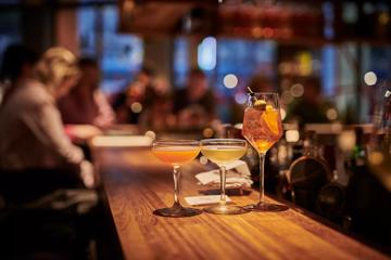 3 drinks focused in the foreground atop the bar and blurred customers in background.