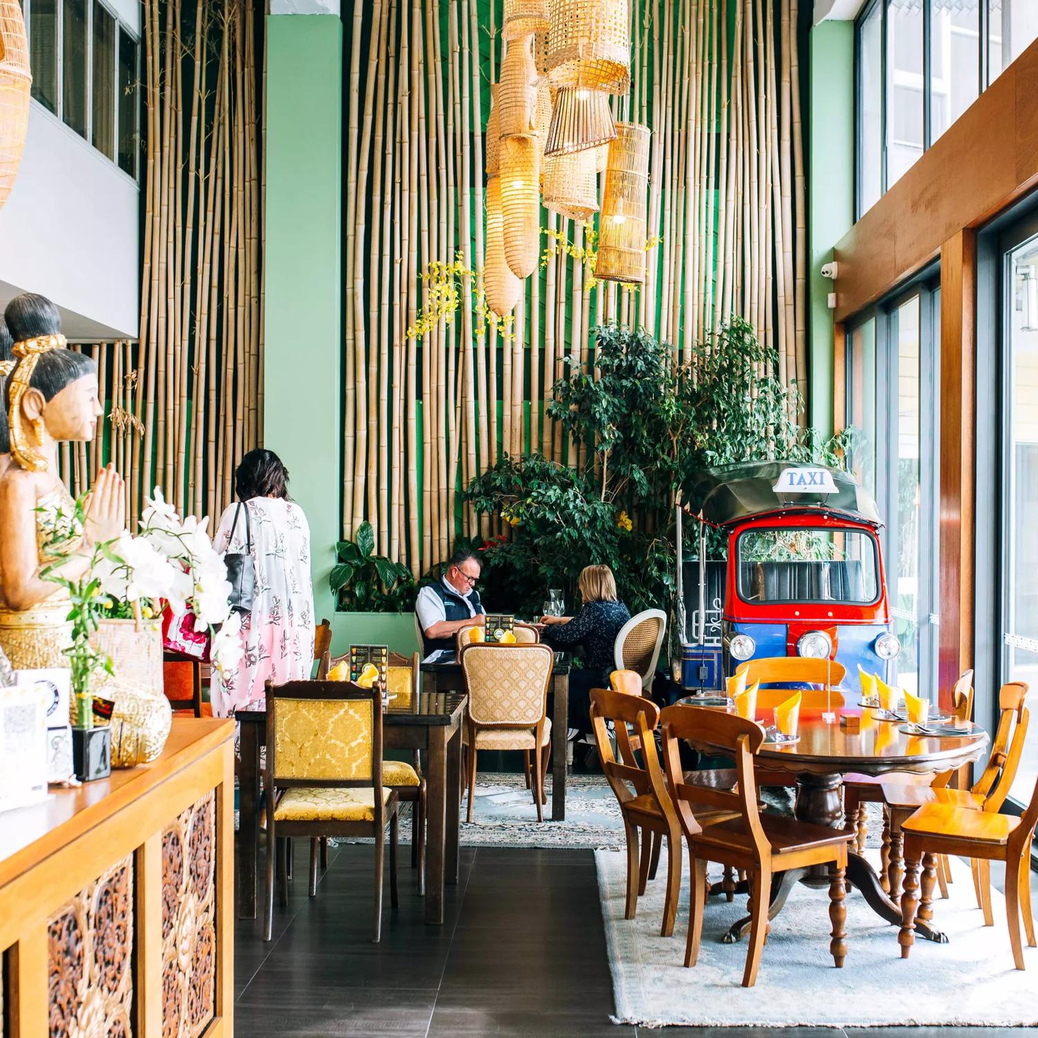 Inside Tuk Tuk Thai Kitchen, a Thai restaurant in Porirua, New Zealand. The bright room has tables, chairs greenery and bamboo accents.