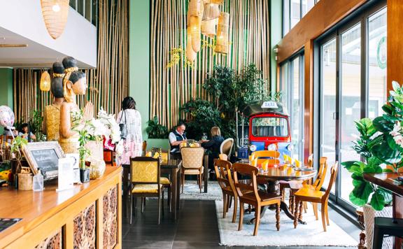 Inside Tuk Tuk Thai Kitchen, a Thai restaurant in Porirua, New Zealand. The bright room has tables, chairs greenery and bamboo accents.