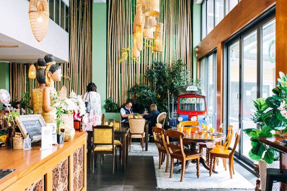 Inside Tuk Tuk Thai Kitchen, a Thai restaurant in Porirua, New Zealand. The bright room has tables, chairs greenery and bamboo accents.