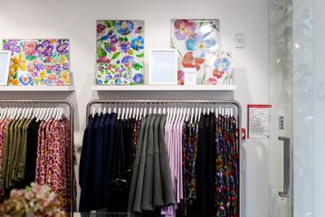 Dresses and jackets hung on white hangers with floral paintings on shelves above in Wilson Trollope.