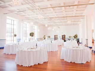 A large bright room, set up for a banquet with round tables with white tablecloths, at Massey University in Wellington, New Zealand.