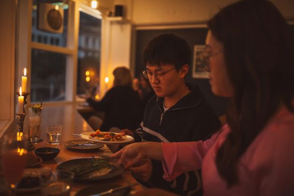 Two friends swapping plates of food inside Supra on Dixon Street. The candlelit room is dim, with people enjoying their meals in the background.