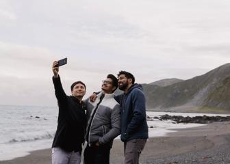 On a cloudy day, three people pose to take a selfie along the beach at Red Rocks Coastal Walkway.