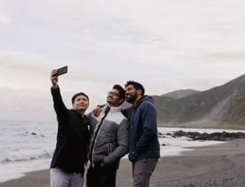 On a cloudy day, three people pose to take a selfie along the beach at Red Rocks Coastal Walkway.