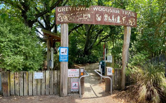 The entrance to the Greytown to Woodside trail. There is a wooden fence, informational signage and a carved sign with the trail's name overhead.