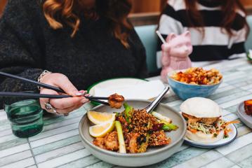 A close-up of three dishes on a table at Mr. Go's. A person uses chopsticks to pick up a prawn from one of the plates.