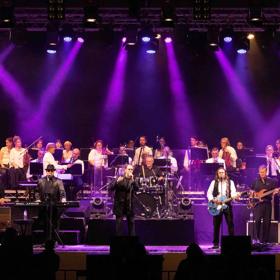 The Best of the Bee Gees Saturday Night Fever and the George Ellis Orchestra perform on stage with purple spotlights.