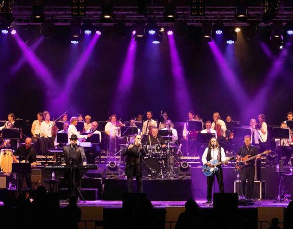 The Best of the Bee Gees Saturday Night Fever and the George Ellis Orchestra perform on stage with purple spotlights.