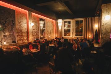 Inside Puffin Wine Bar in Wellington. The space has concrete floors, exposed brick walls, and low lighting. The tables and booths are filled with people enjoying a drink.