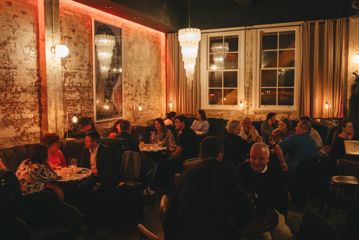 Inside Puffin Wine Bar in Wellington. The space has concrete floors, exposed brick walls, and low lighting. The tables and booths are filled with people enjoying a drink.